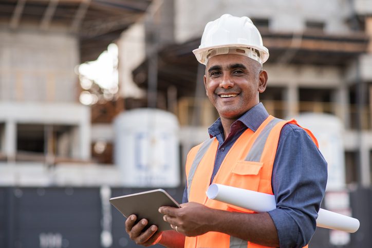 Minority Construction business owner using a tablet and holding blueprints