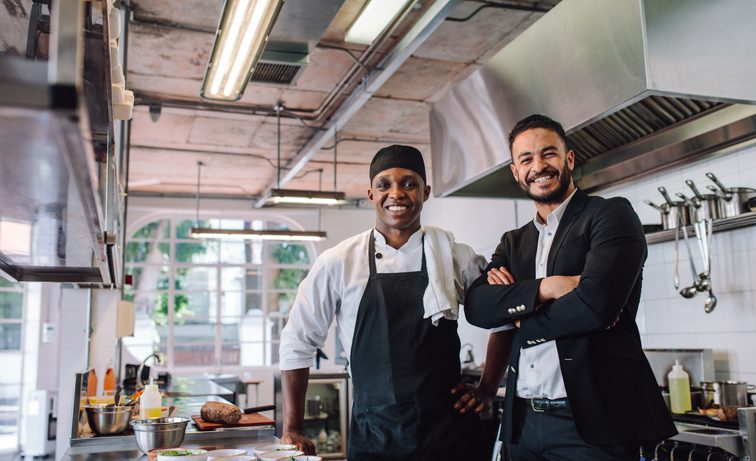 Restaurant owner with chef standing in kitchen smiling