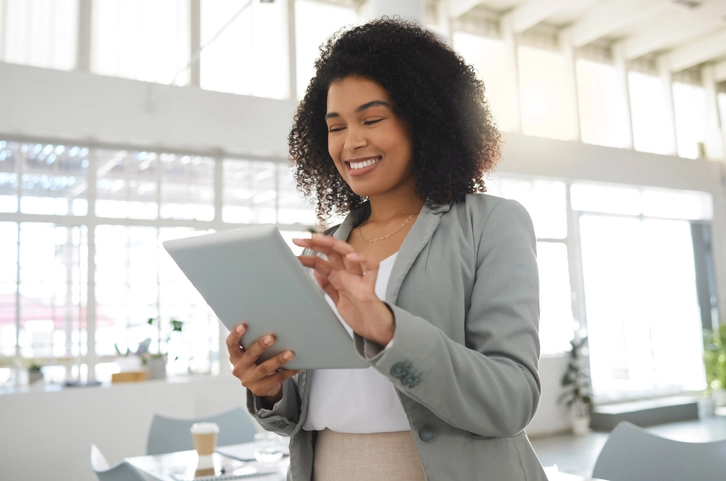 Mixed-race business owner smiling while looking at her tablet. She is preparing to fill out the SBA Form 413