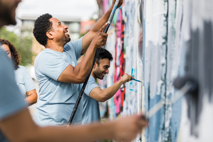 Group of people smiling while painting a wall, benefiting from the Community Reinvestment Act.
