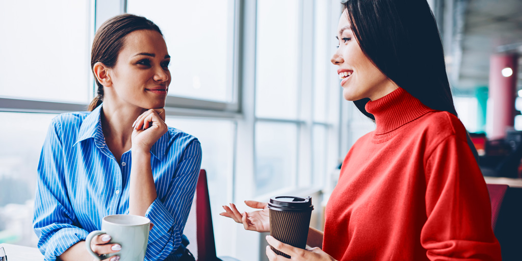 Generic office with two women talking over coffee.