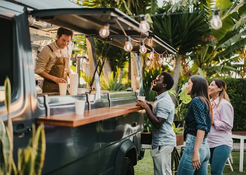 Group of three young adults ordering from a food truck surrounded by greenery